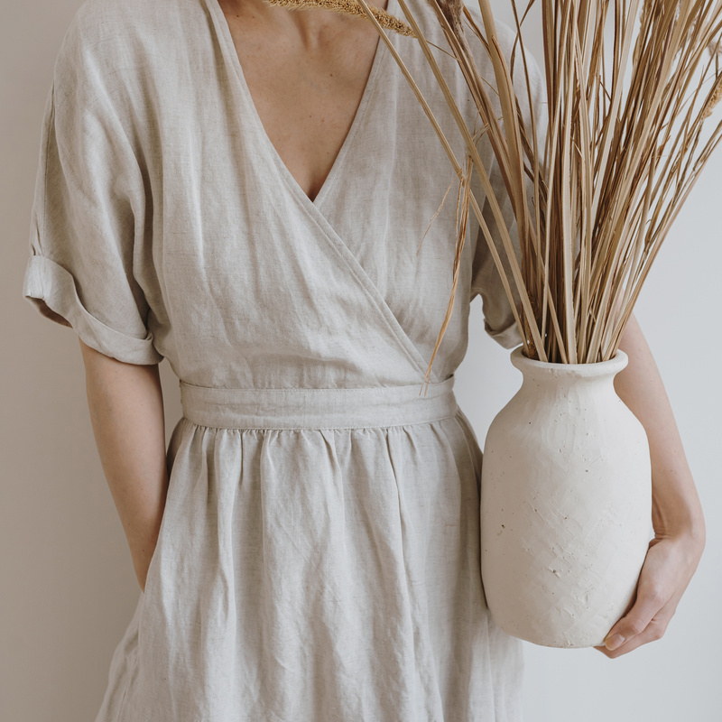 Woman in Beige Dress Holding a Vase with Dried Plants